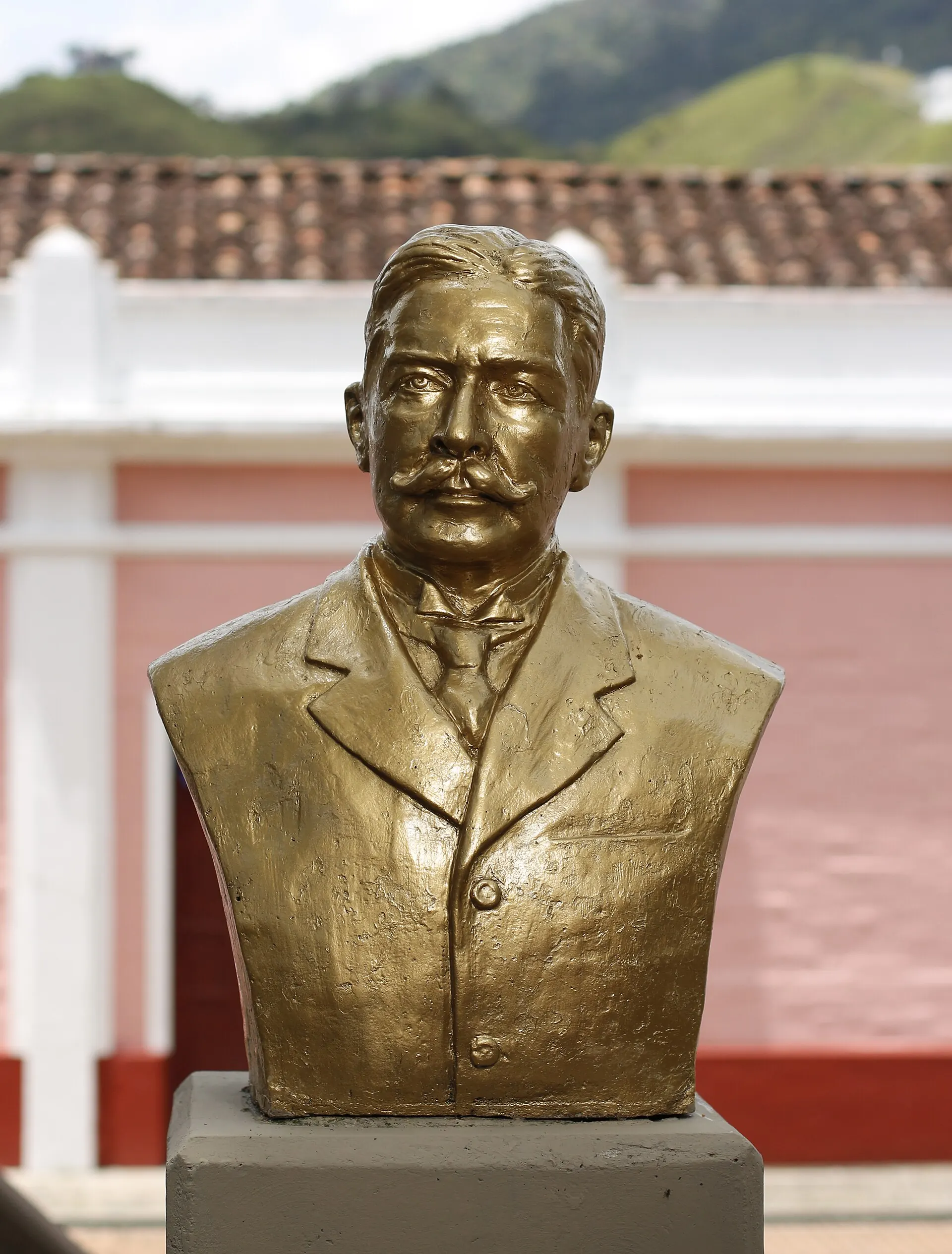 Busto de bronce de un hombre sobre un pedestal, contra una fachada rosada