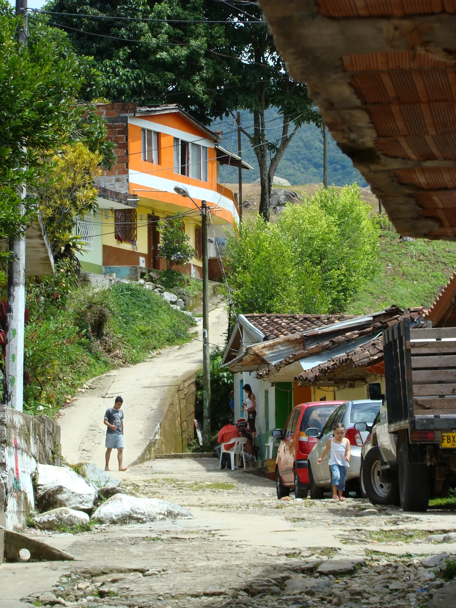 Calle empinada sin pavimentar entre casas, con un camión y un peatón.
