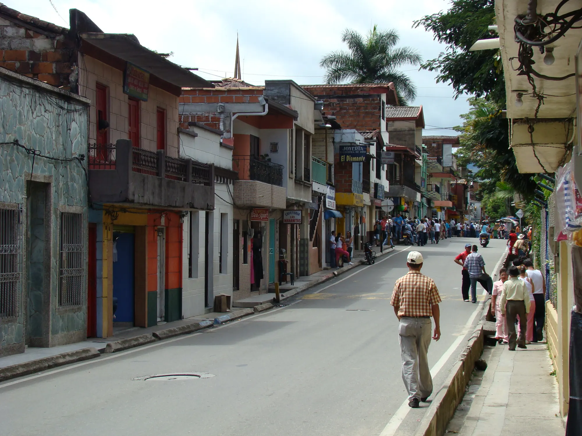 Calle de casas de dos pisos con balcones de colores que lleva al parque; al fondo, la torre de la iglesia.