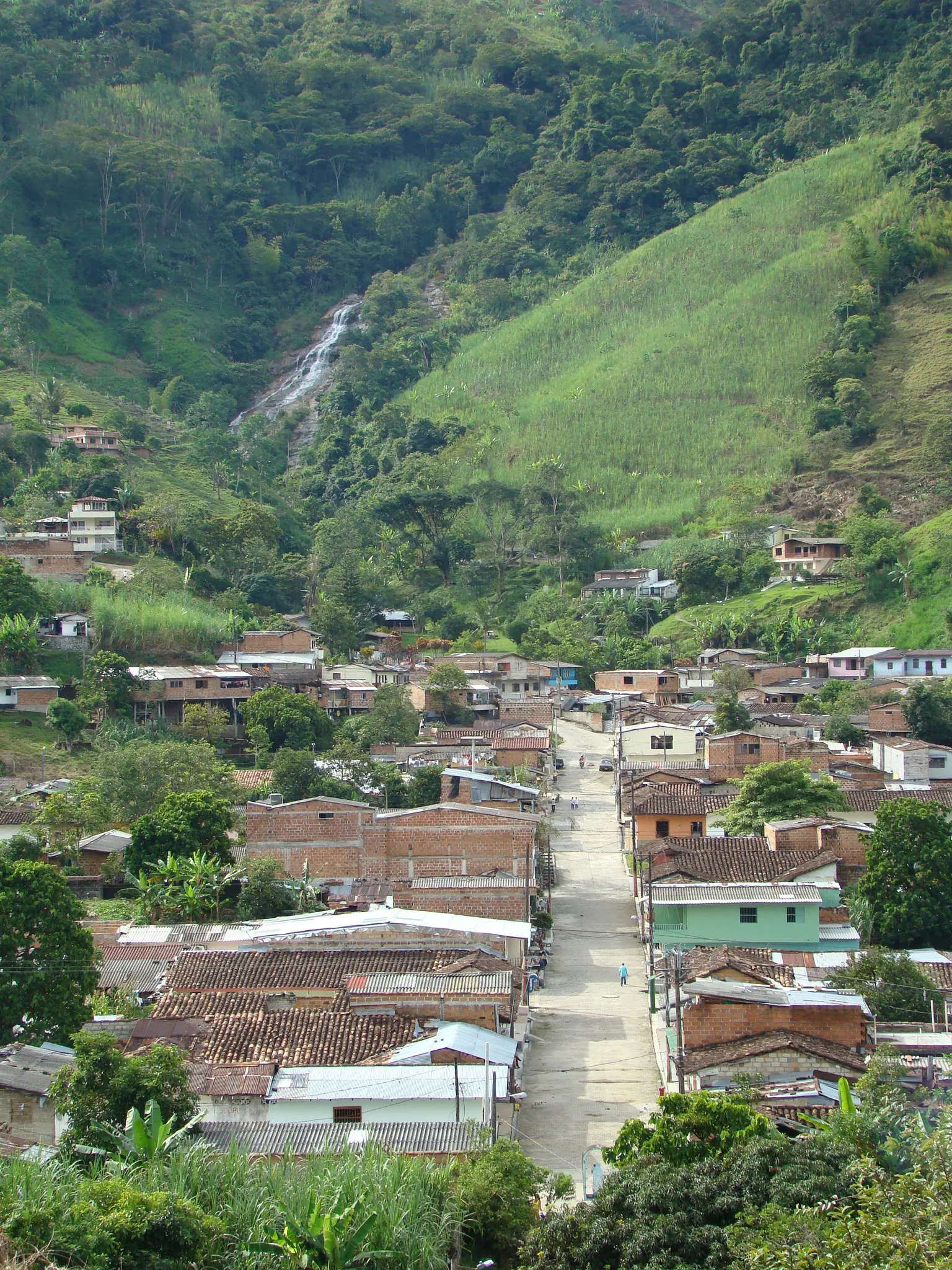El pueblo desde lo alto: una calle recta que sube hacia la montaña y, arriba, una cascada que baja por la ladera.