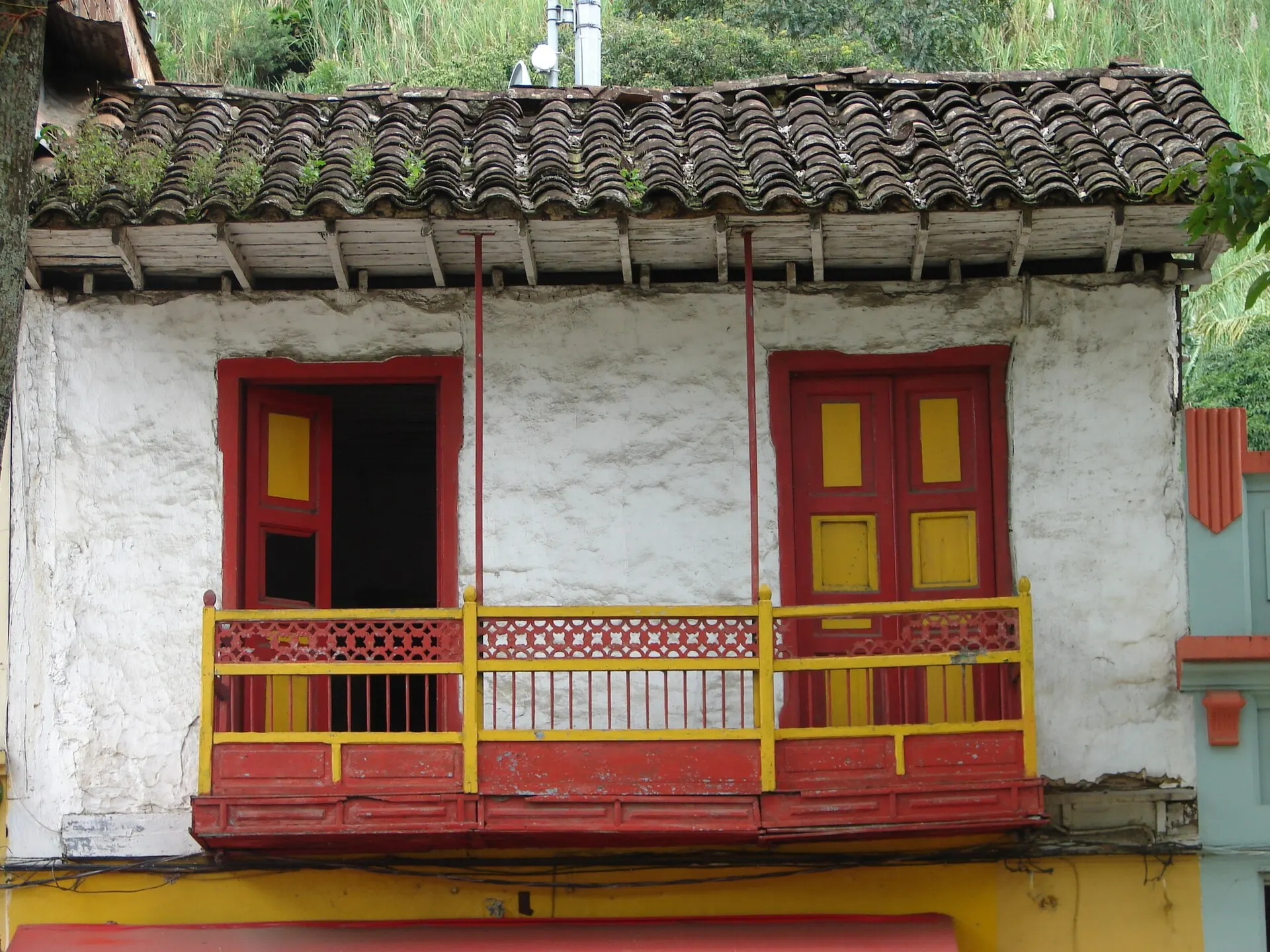 Fachada de casa antigua de tapia con balcón de madera rojo y amarillo y alero de teja de barro.