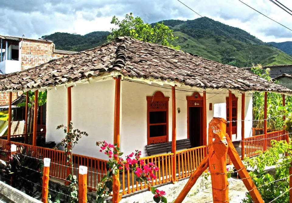 Casa campesina tradicional con corredor, chambranas naranjas, flores y techo de teja de barro.