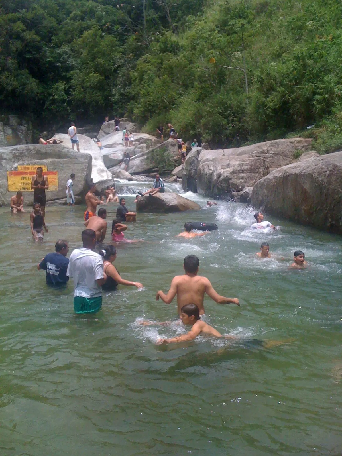 Bañistas en el charco La Plancha, una poza de agua clara entre rocas y vegetación.