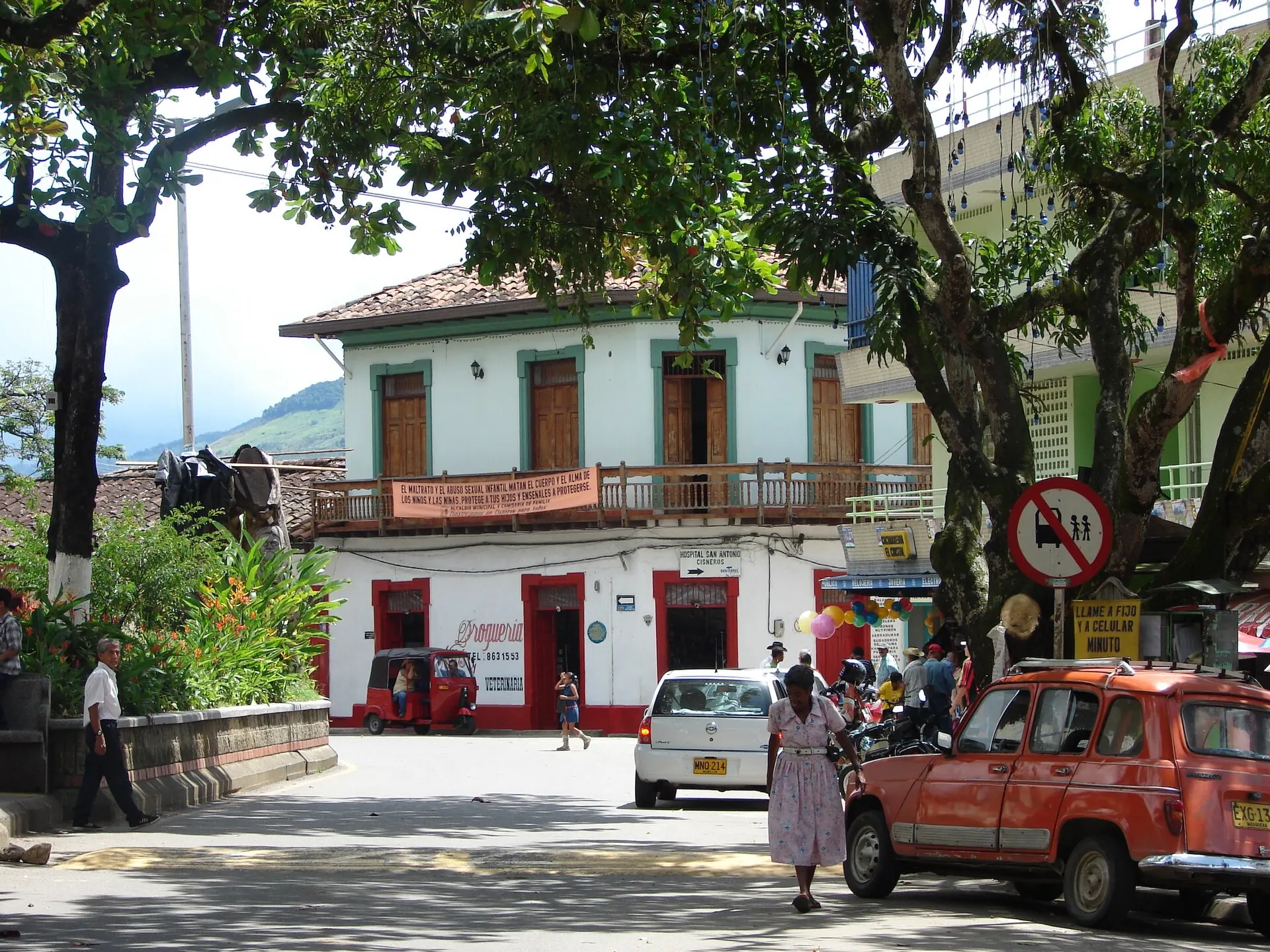 Esquina del centro con casa de balcón corrido, árboles y carros antiguos.