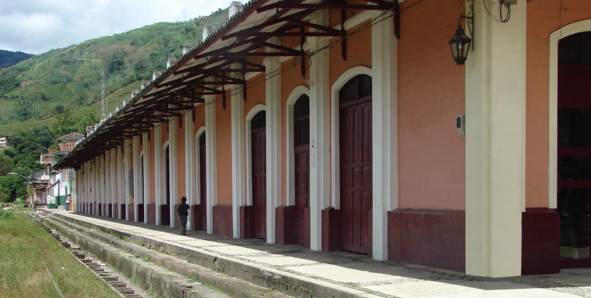 Andén y fachada lateral de la antigua estación del ferrocarril de Cisneros: arcos, puertas de madera y alero sobre la vía.
