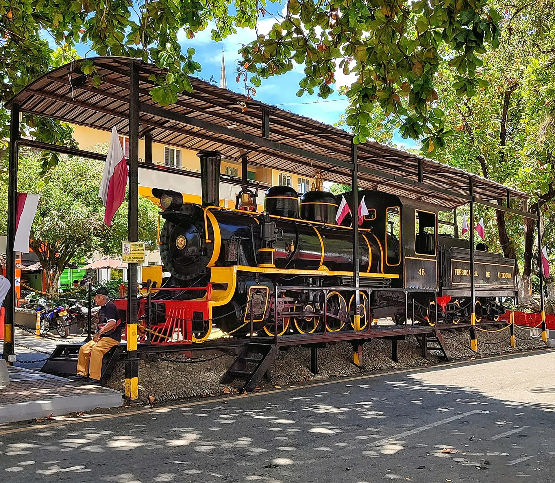La locomotora de vapor n.º 45 restaurada, negra con detalles rojos y dorados, bajo su cubierta en el parque, con banderas.