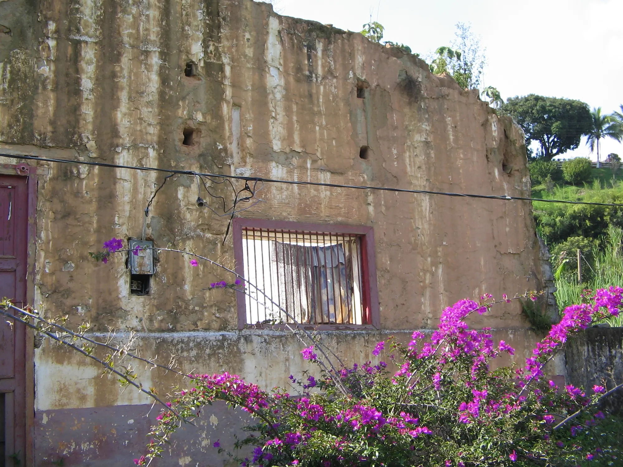 Muro de una antigua bodega del ferrocarril con una ventana enrejada y buganvilla florecida.