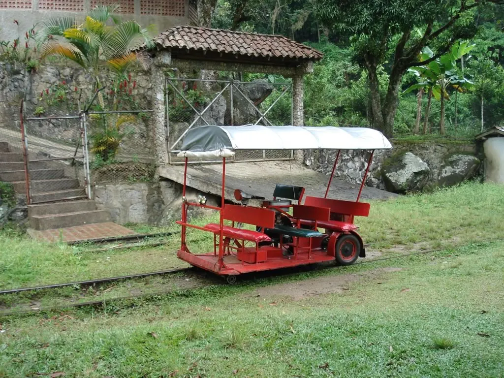 Vehículo artesanal rojo sobre rieles («moto-mesa») con toldo, junto a un andén con escaleras.