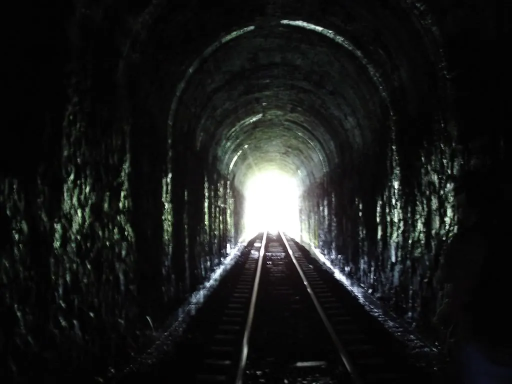 Bóveda de piedra del túnel con los rieles hacia la boca iluminada